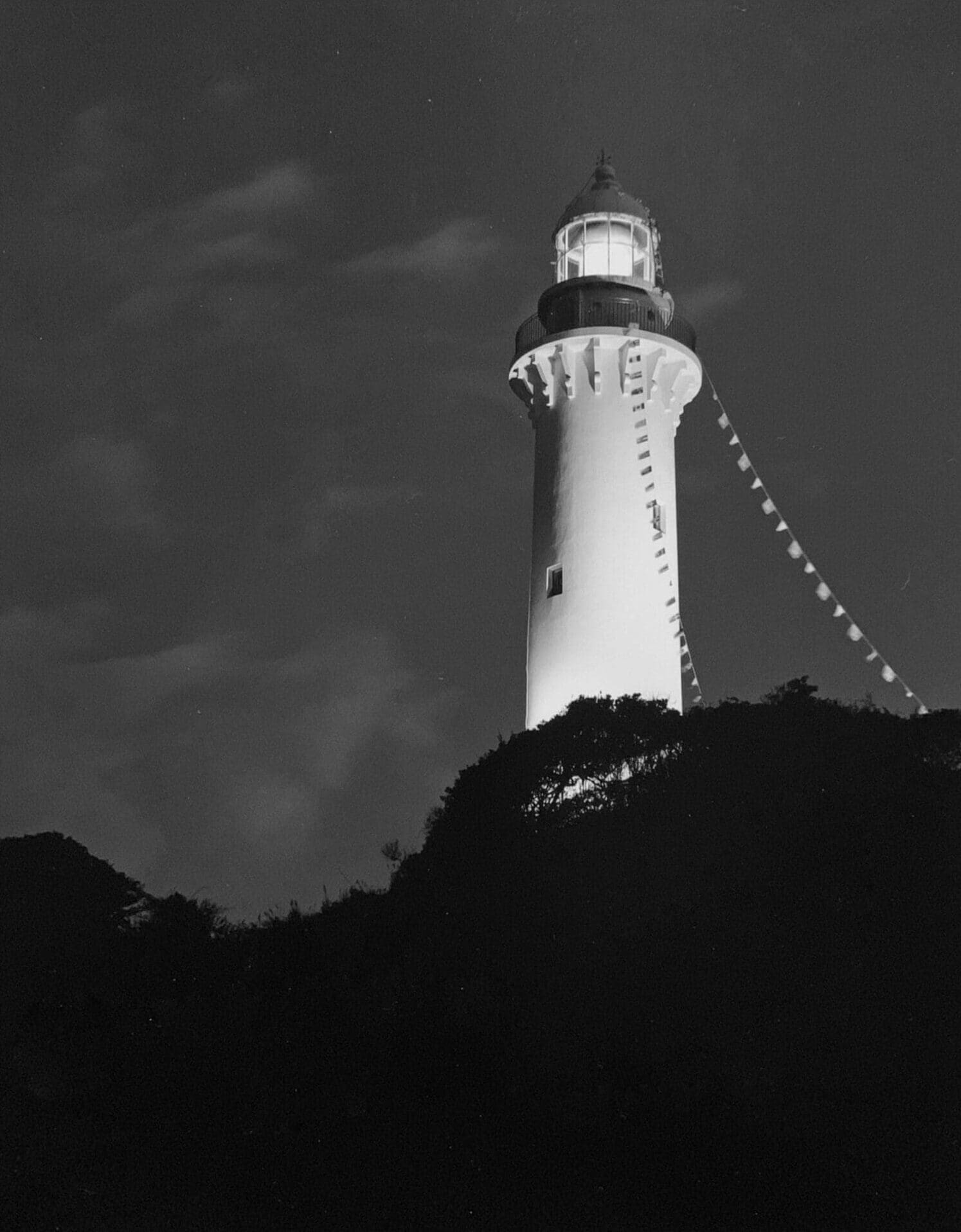 Shioyasaki Lighthouse lit at twilight above a dark hill, Iwaki, Japan — minimalist lighthouse print in black and white