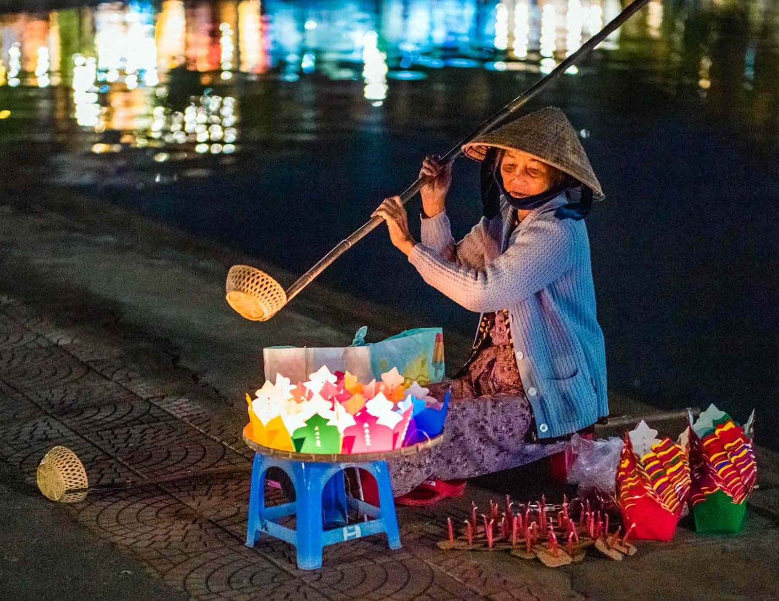 Enchanting Nighttime Lantern Vendor by Vietnam Riverside A Hoi An Vietnamese vendor selling colorful lanterns by a reflective river at night.