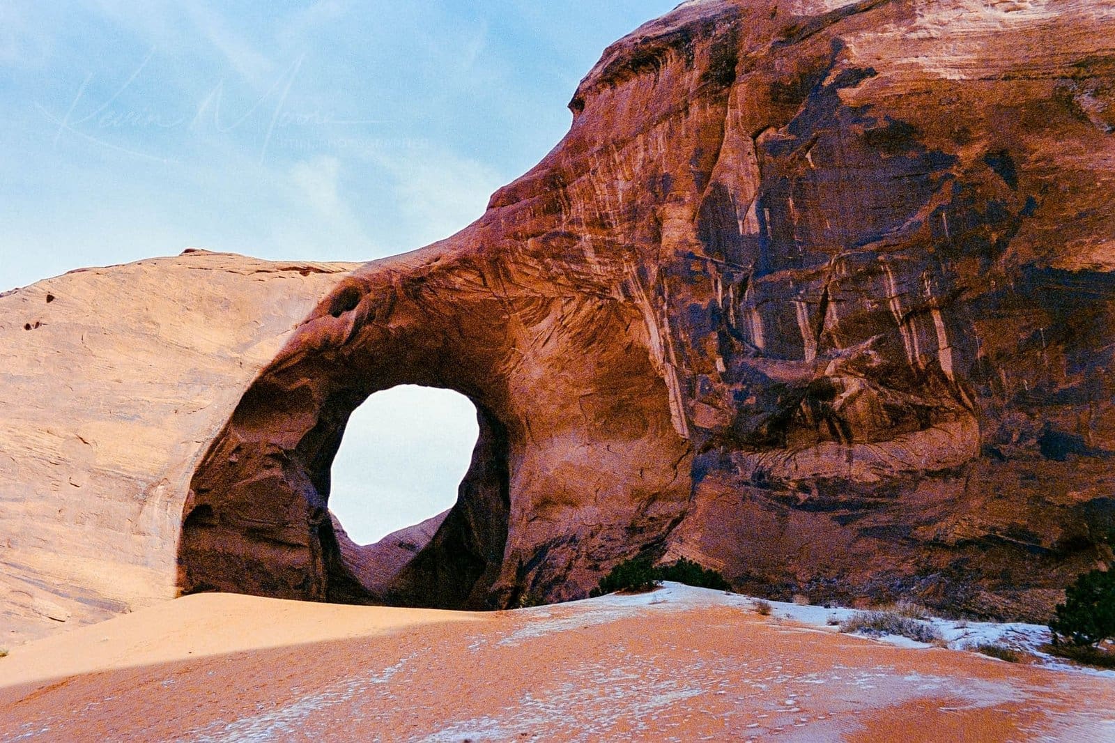 Sunlit sandstone arch against clear blue sky at sunrise or sunset.