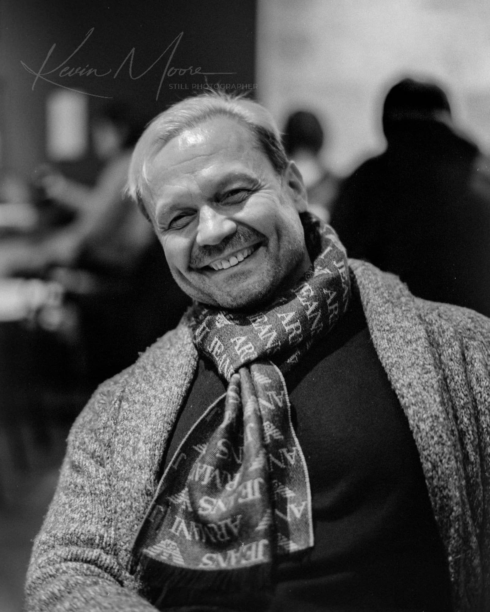 Cheerful middle-aged man in winter attire in cosy indoor setting.