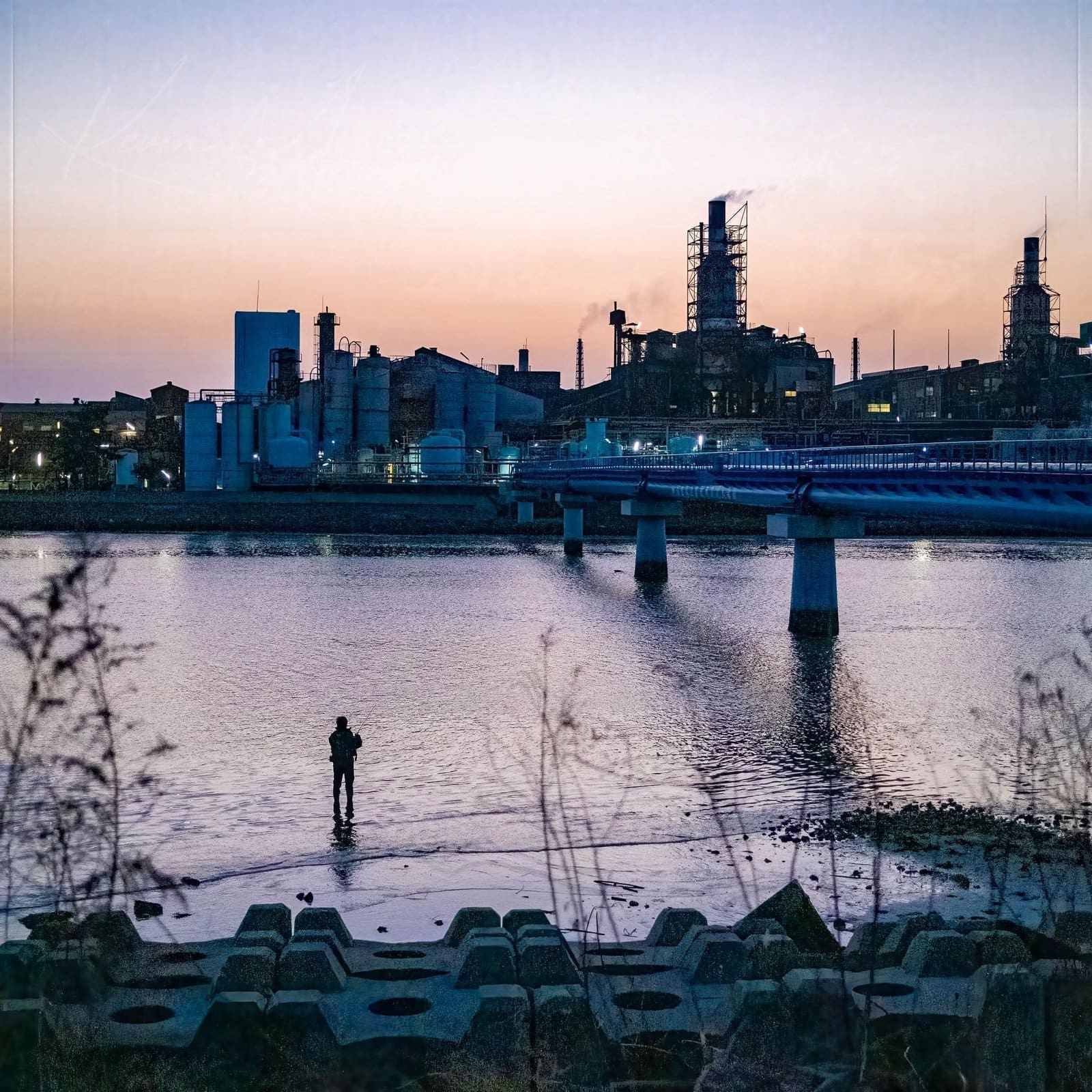 Twilight Solitude Solitary figure fishing by a serene inlet against a twilight industrial cityscape.