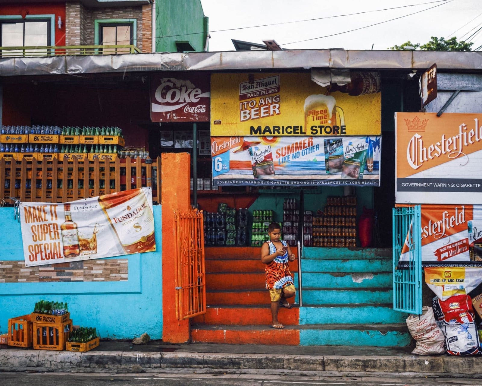 Daily Life at the Colorful Maricel Store in the Philippines Colorful Maricel Store front with local boy and product crates in a Filipino street scene.