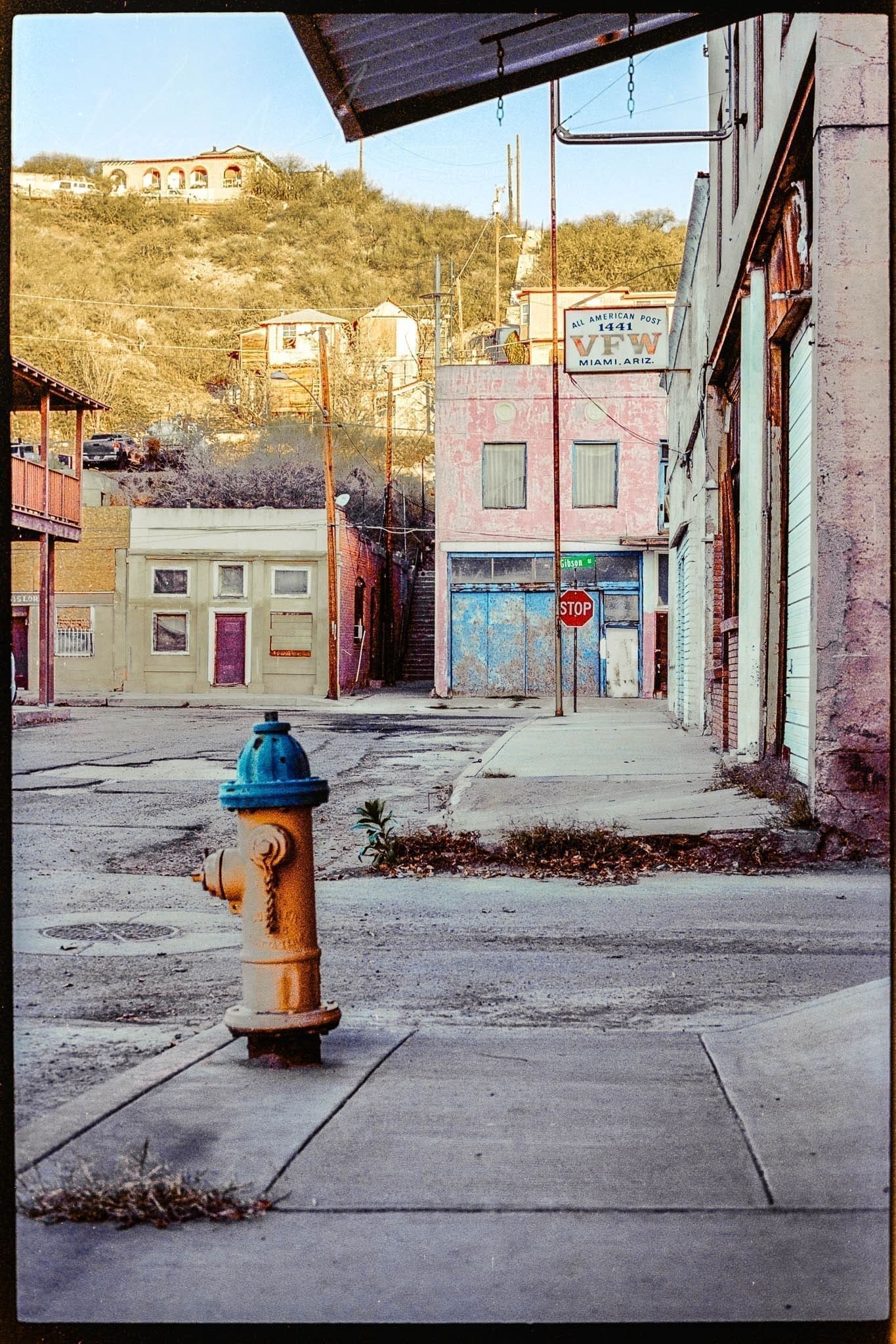 Vibrant fire hydrant standing out in a serene, weathered town nestled in hilly landscape.