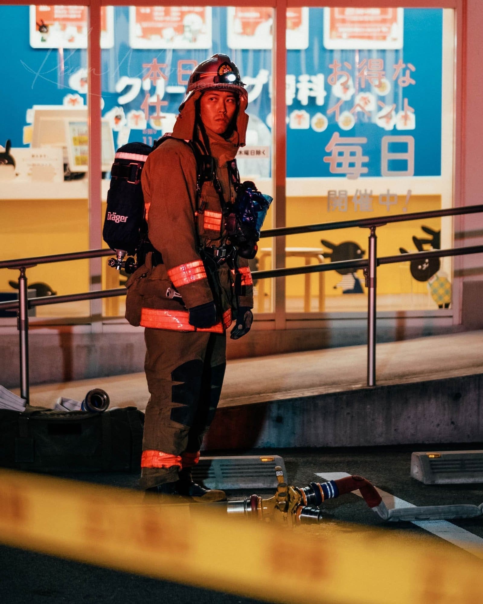 Urban Night: Firefighter Amidst Contrasting City Lights Firefighter in gear at nighttime with vivid ads in urban Japan.