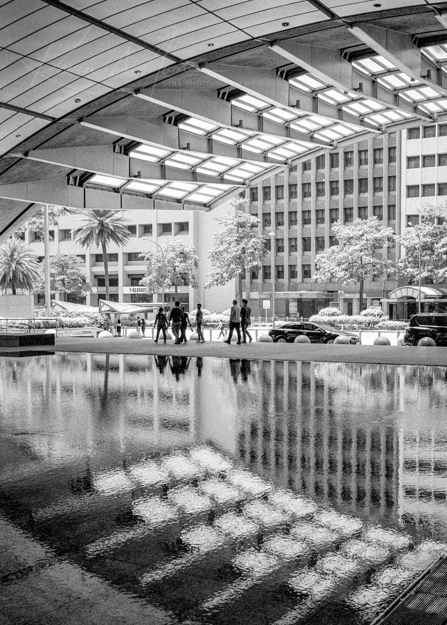 Modern urban plaza with geometric ceiling, palm trees, and reflective pool.