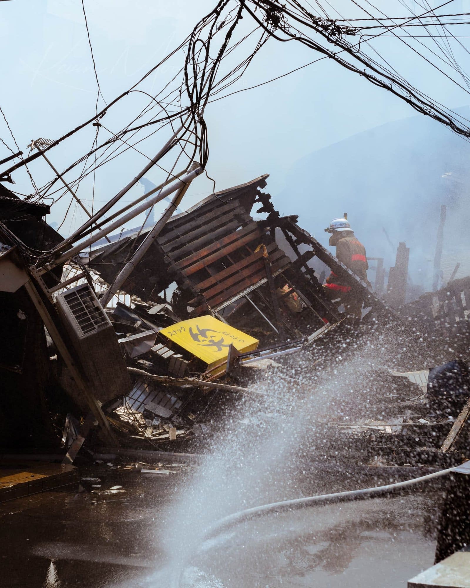 Emergency worker manages disaster scene with debris and water spray.