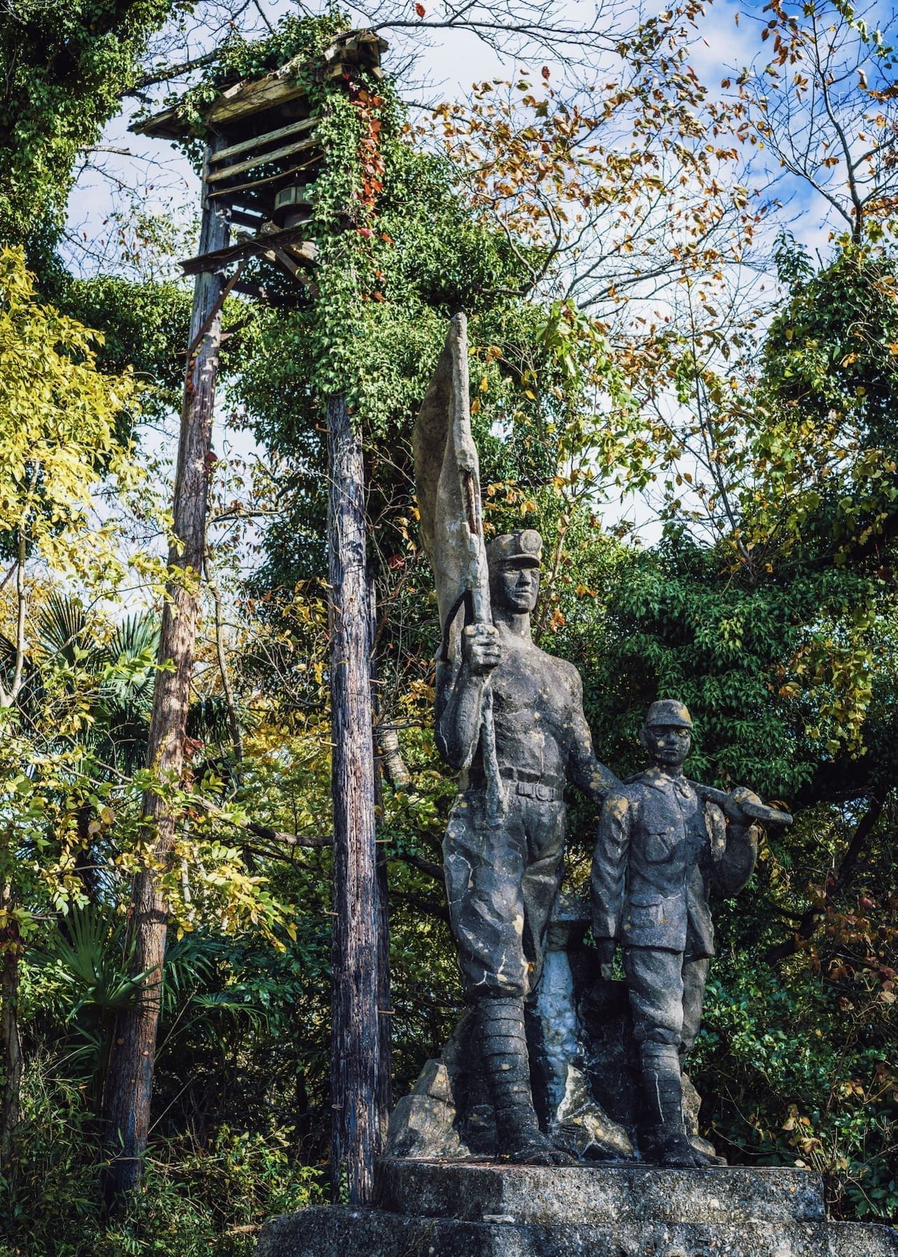 Bronze statue of soldiers amidst lush greenery and historical watchtower.