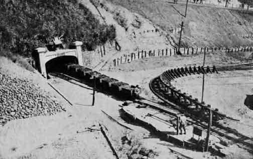 Historic train emerging from tunnel in early 20th-century mining scene.