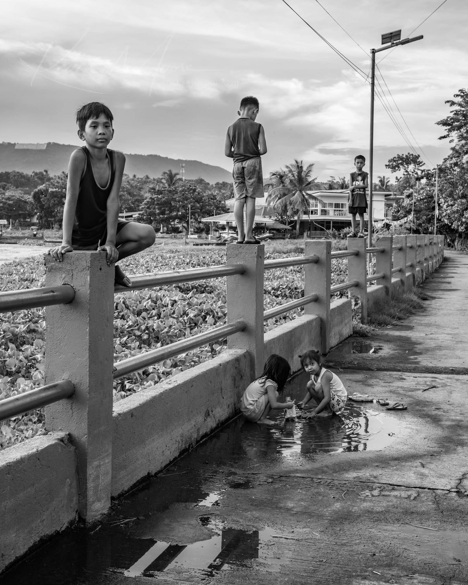 Rural Bridge Life: Filipino Children Play and Contemplation Filipino children playing on a rural bridge with scenic backdrop.